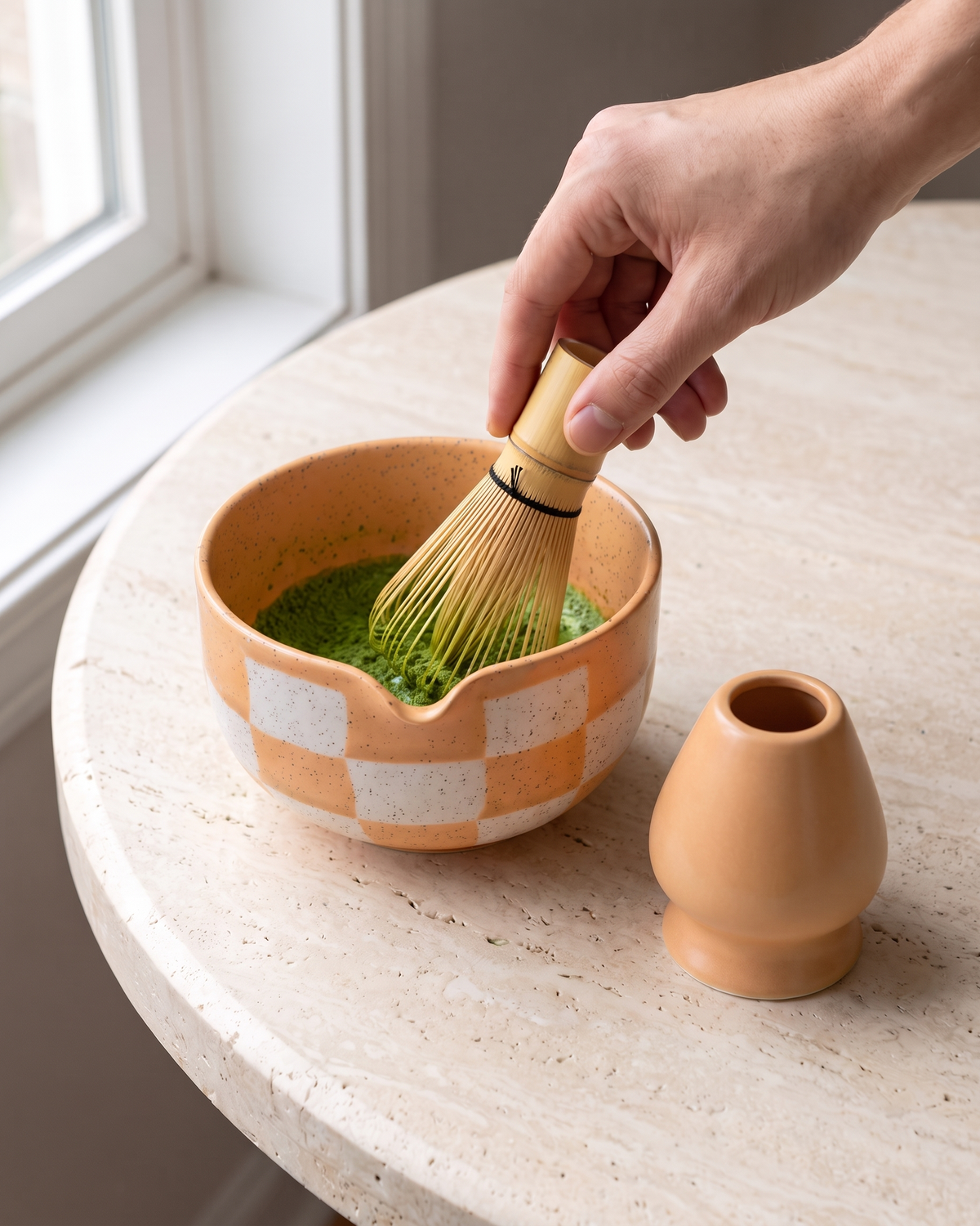 In use: 2-Piece Checkerboard Bowl & Holder Set – Apricot, hand whisking matcha in the bowl with a bamboo whisk (sold separately), holder beside