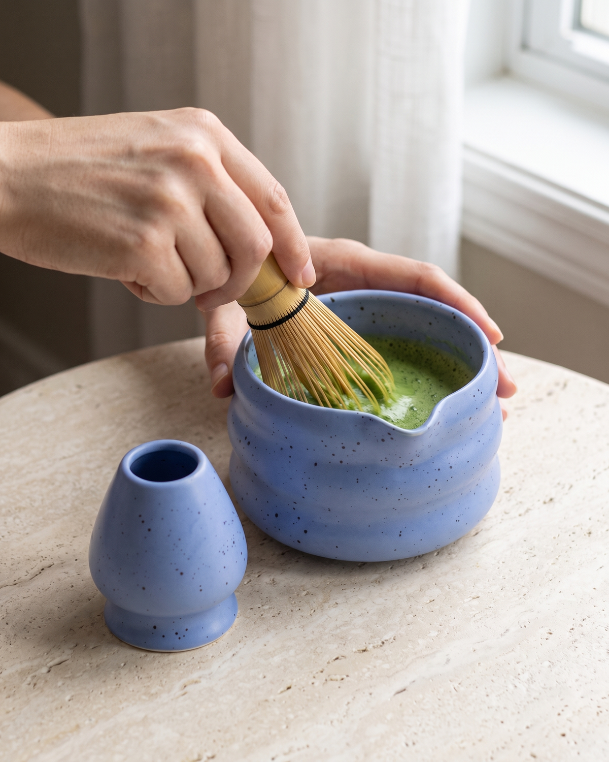 In use: 2-Piece Speckled Matcha Bowl & Holder Set – Blue, hand whisking matcha in the bowl with a bamboo whisk (sold separately), holder beside