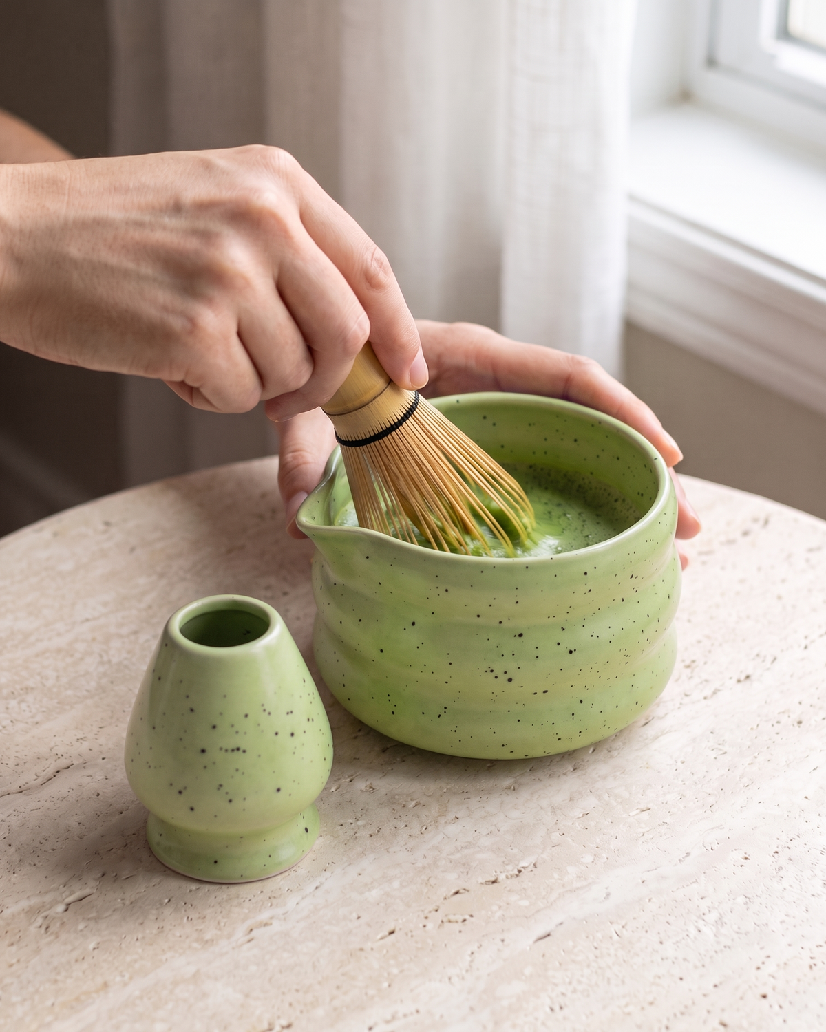 In use: 2-Piece Speckled Matcha Bowl & Holder Set – Green, hand whisking matcha in the bowl with a bamboo whisk (sold separately), holder beside