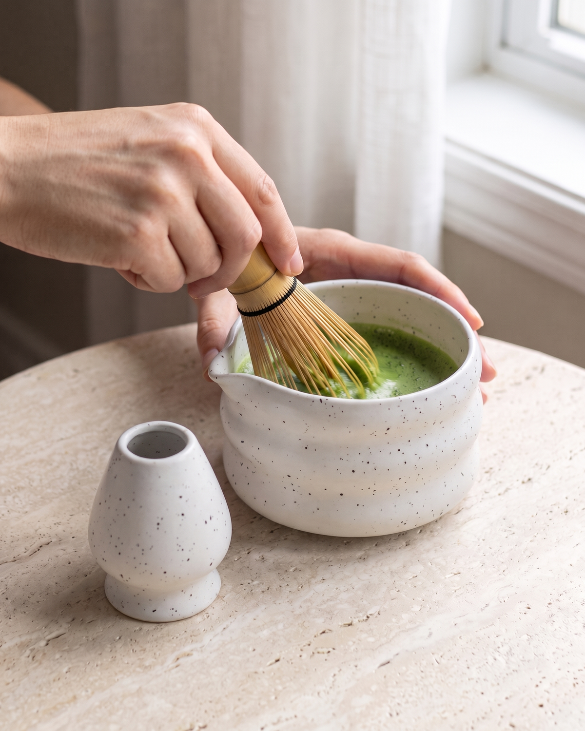 In use: 2-Piece Speckled Matcha Bowl & Holder Set – White, hand whisking matcha in the bowl with a bamboo whisk (sold separately), holder beside