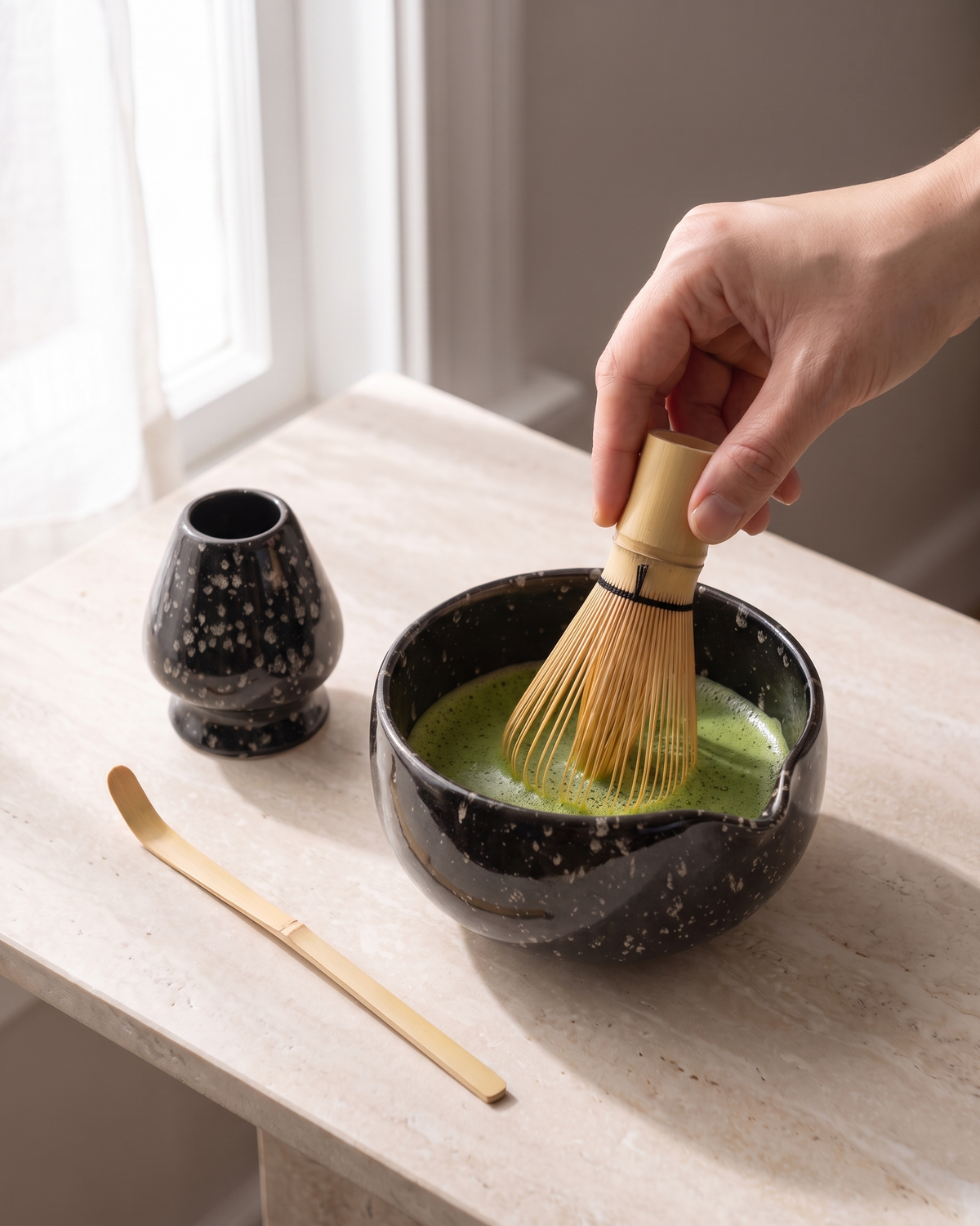 In use: 5-Piece Patterned Matcha Set with Bowl, Whisk, Holder, Scoop & Sifter – Speckled Black, hand whisking matcha in the bowl, holder and scoop beside