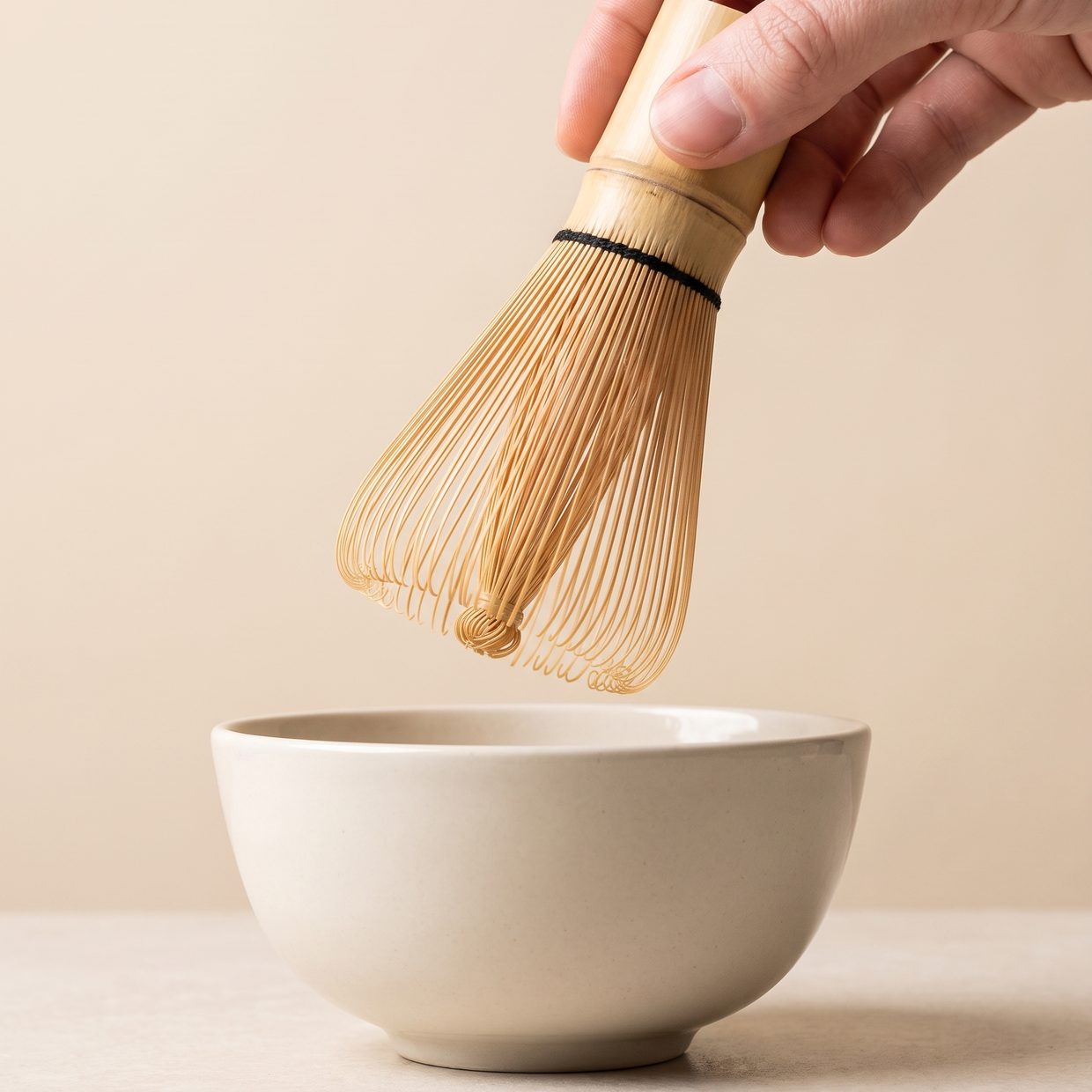 Hand lowering a bamboo matcha whisk into a ceramic bowl